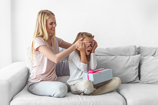 madre che copre con le sue mano gli occhi alla figlia sedute su un divano